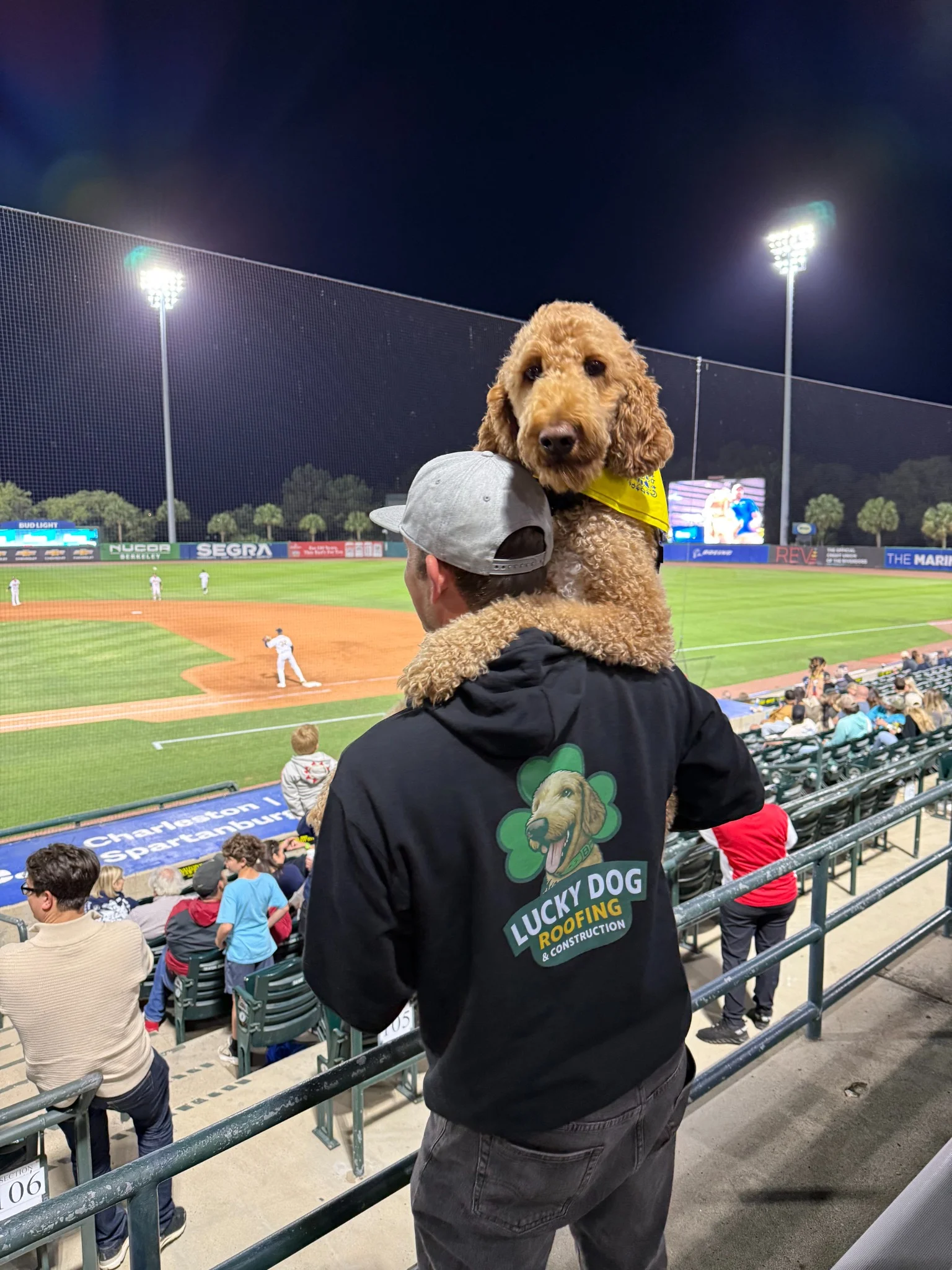 Brad wearing his Lucky Dog jacket at a local baseball game, with Tucker looking over his shoulder