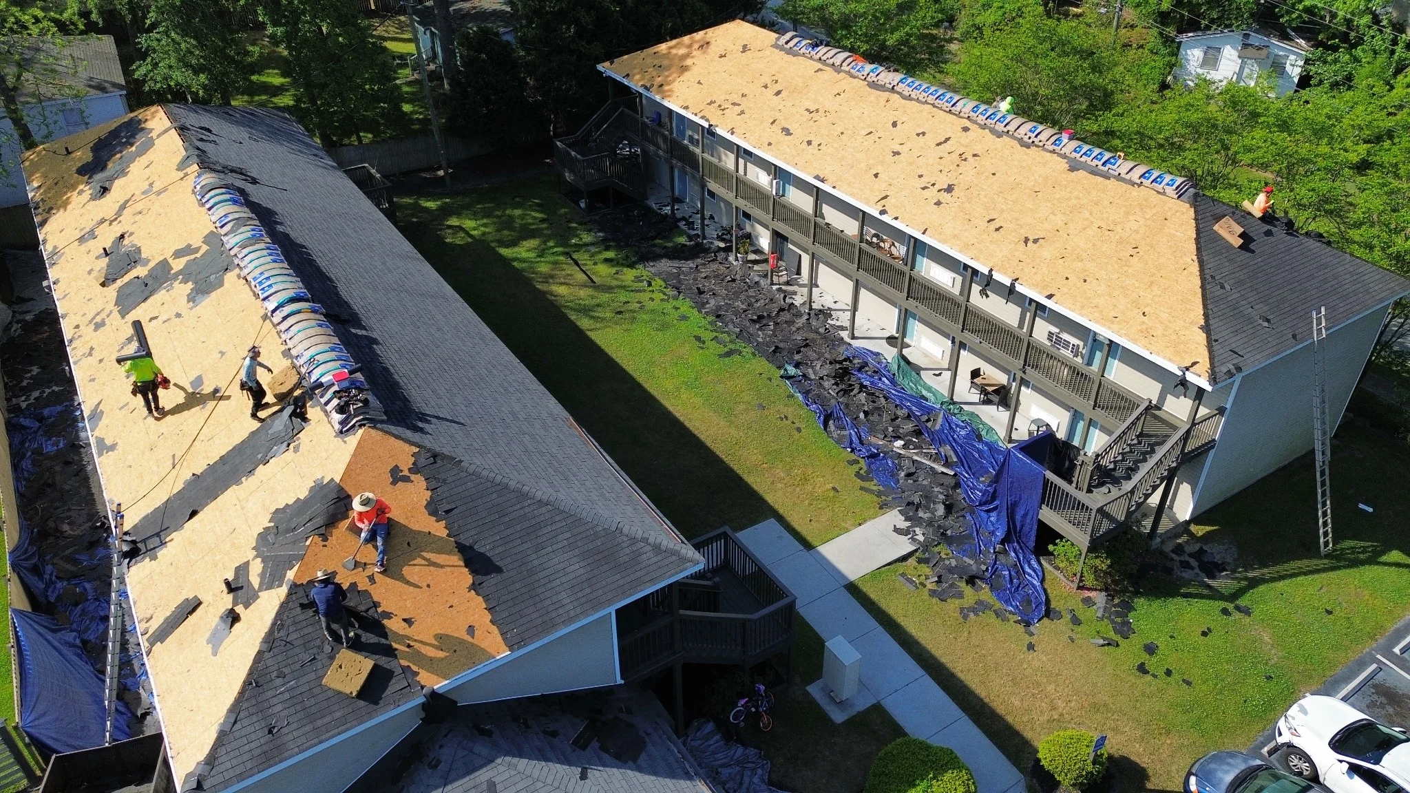 Roof replacement in progress across two multifamily buildings, showing tear-off, exposed decking and shingle installation